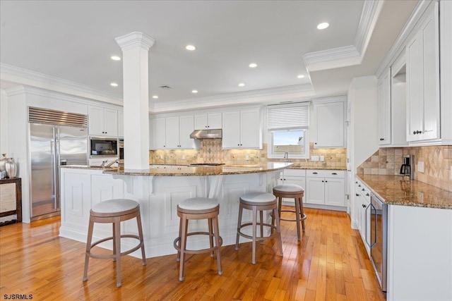 kitchen featuring white cabinetry, a kitchen island, built in appliances, and dark stone countertops