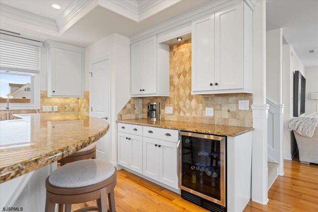 kitchen with white cabinetry, light wood-type flooring, beverage cooler, and light stone counters