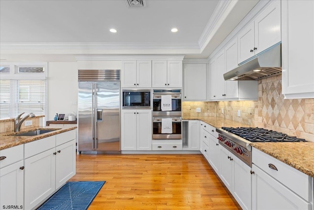 kitchen featuring ornamental molding, built in appliances, white cabinets, and light stone counters