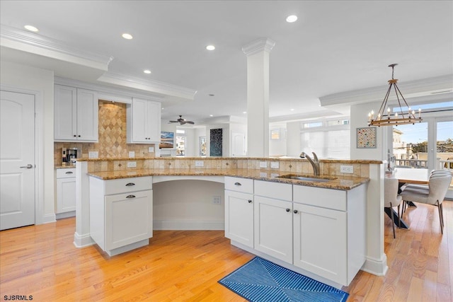 kitchen featuring sink, white cabinets, hanging light fixtures, ornamental molding, and light stone counters