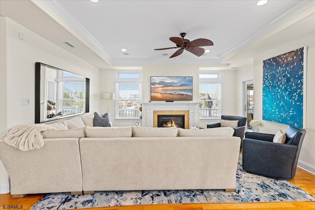 living room featuring hardwood / wood-style flooring, ornamental molding, ceiling fan, and a tray ceiling