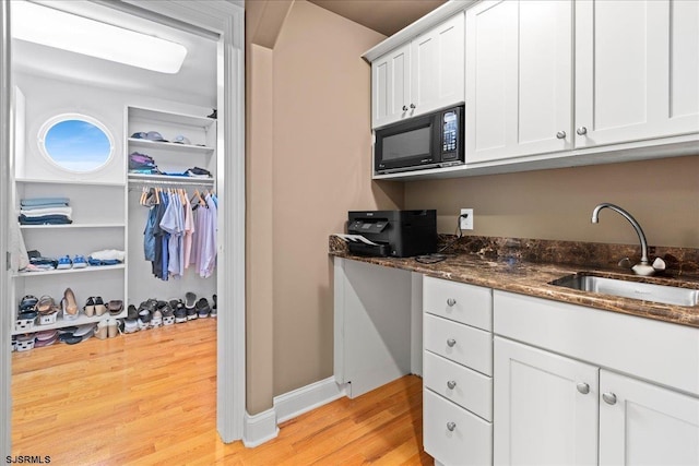 kitchen featuring white cabinetry, dark stone counters, light hardwood / wood-style floors, and sink