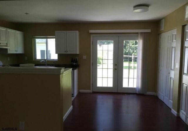 kitchen with french doors, dark wood-type flooring, kitchen peninsula, range hood, and white cabinets