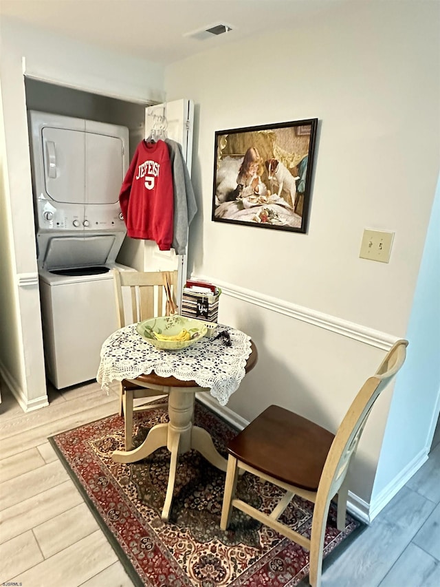 laundry room with laundry area, stacked washer and clothes dryer, baseboards, and wood finished floors