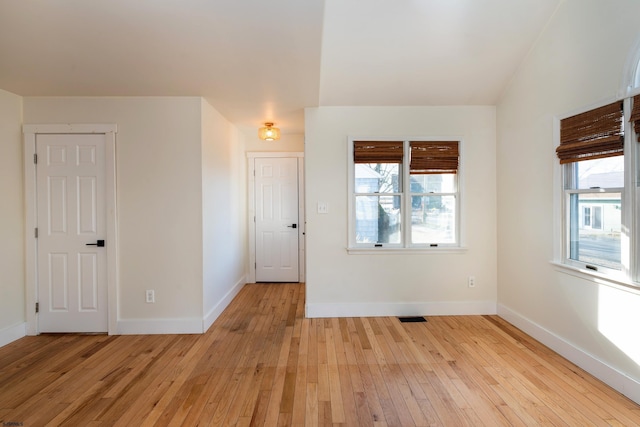 empty room featuring a wealth of natural light, vaulted ceiling, and light wood-type flooring