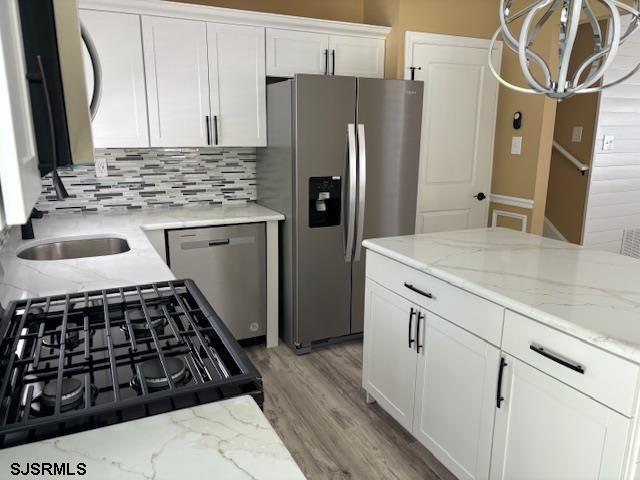 kitchen with white cabinetry, backsplash, stainless steel appliances, light stone counters, and light wood-type flooring