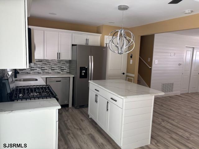 kitchen featuring a kitchen island, decorative light fixtures, white cabinetry, wood-type flooring, and stainless steel appliances