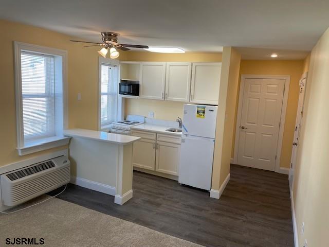 kitchen with an AC wall unit, white cabinets, dark hardwood / wood-style flooring, kitchen peninsula, and white appliances