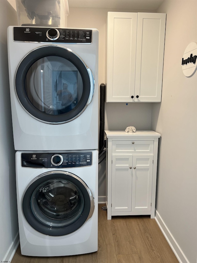 clothes washing area with stacked washer / dryer, cabinets, and light hardwood / wood-style flooring