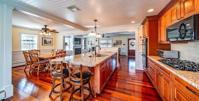 kitchen with light stone counters, sink, an island with sink, and black appliances