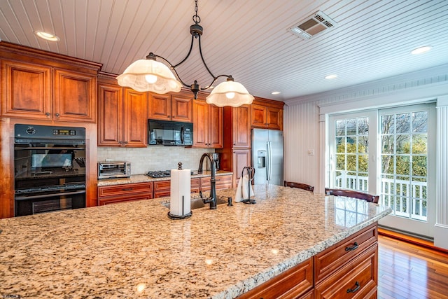 kitchen featuring hanging light fixtures, light stone countertops, light hardwood / wood-style floors, decorative backsplash, and black appliances