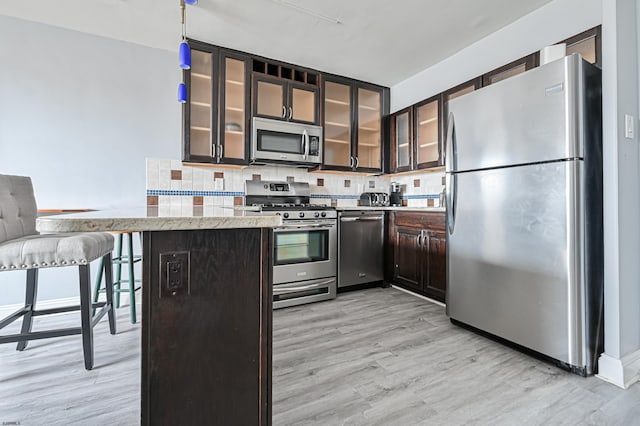 kitchen featuring decorative backsplash, kitchen peninsula, stainless steel appliances, dark brown cabinets, and light wood-type flooring