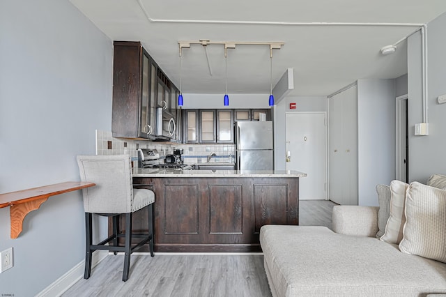 kitchen featuring tasteful backsplash, dark brown cabinets, light wood-type flooring, kitchen peninsula, and stainless steel appliances