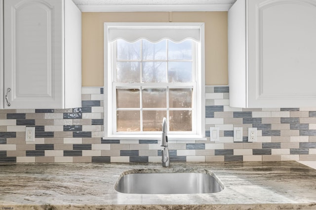 kitchen with light stone countertops, sink, white cabinets, and backsplash