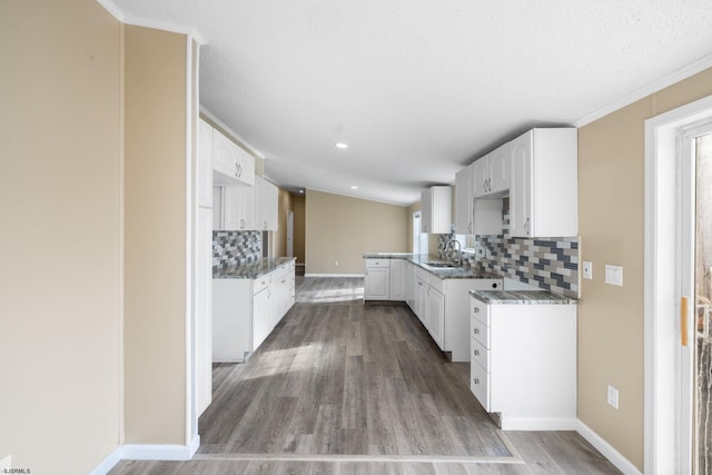 kitchen featuring white cabinetry, sink, decorative backsplash, hardwood / wood-style flooring, and dark stone counters