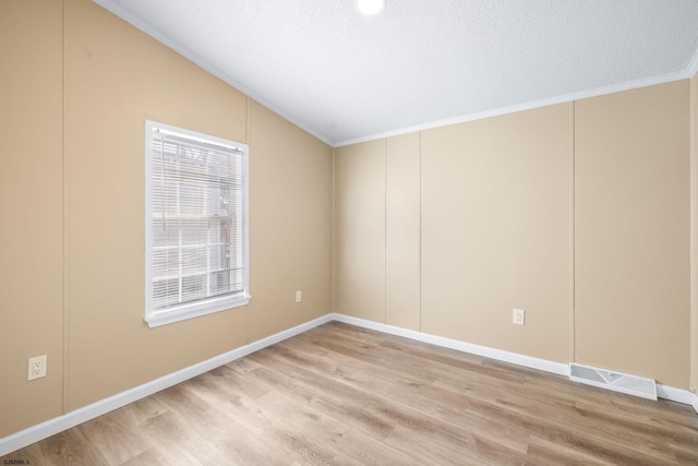 empty room with vaulted ceiling, crown molding, a textured ceiling, and light wood-type flooring