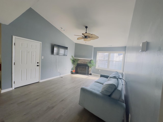 living room featuring a stone fireplace, wood-type flooring, ceiling fan, and vaulted ceiling