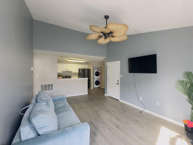 living room featuring ceiling fan, lofted ceiling, stacked washing maching and dryer, and light wood-type flooring