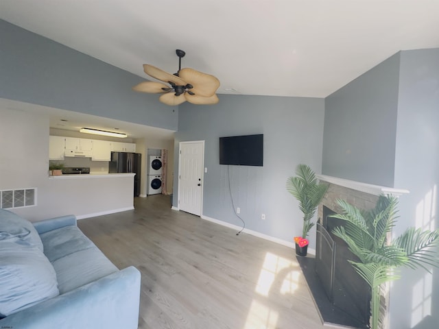 living room featuring vaulted ceiling, a fireplace, stacked washer and dryer, ceiling fan, and light hardwood / wood-style flooring