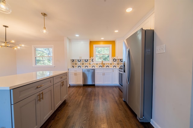 kitchen with appliances with stainless steel finishes, pendant lighting, tasteful backsplash, white cabinets, and dark wood-type flooring