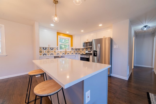 kitchen with appliances with stainless steel finishes, pendant lighting, white cabinets, decorative backsplash, and a center island