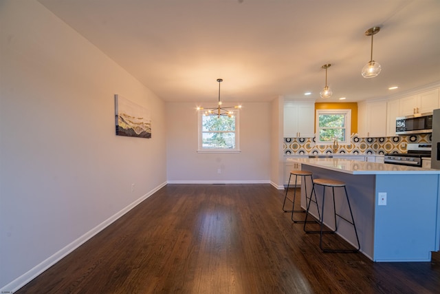 kitchen featuring a breakfast bar, appliances with stainless steel finishes, white cabinetry, hanging light fixtures, and decorative backsplash