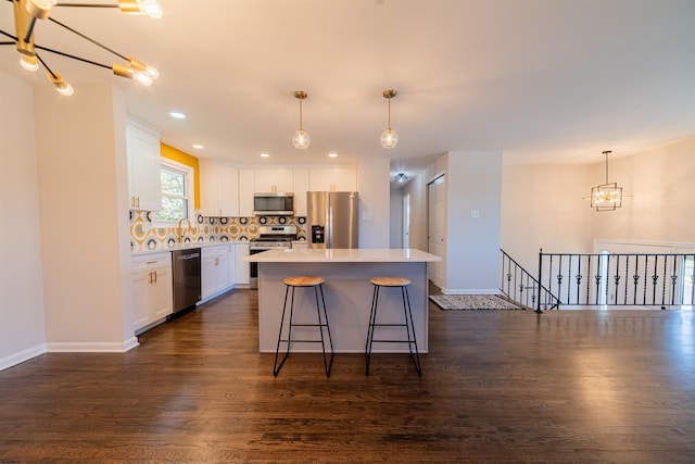 kitchen featuring dark wood-type flooring, white cabinetry, appliances with stainless steel finishes, a kitchen island, and pendant lighting