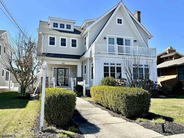 shingle-style home featuring covered porch, a balcony, and a front yard