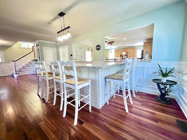 kitchen featuring a breakfast bar area, hanging light fixtures, dark hardwood / wood-style floors, kitchen peninsula, and ceiling fan