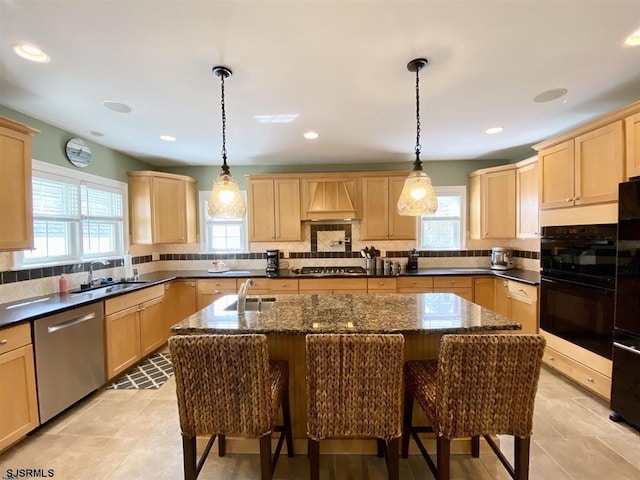 kitchen featuring decorative light fixtures, black appliances, an island with sink, and light brown cabinets