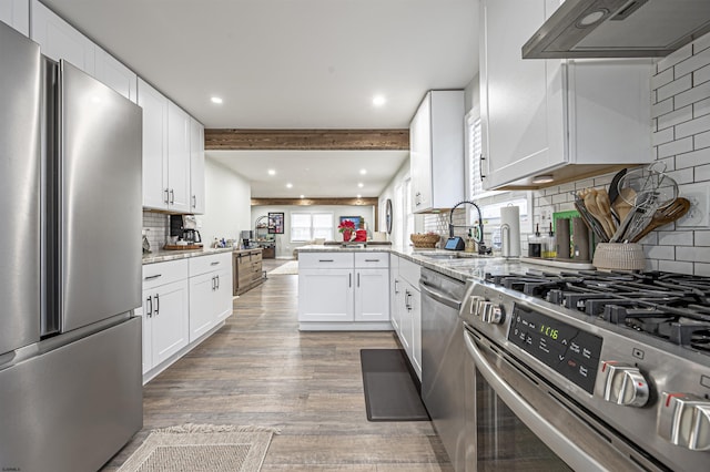 kitchen with appliances with stainless steel finishes, sink, white cabinets, kitchen peninsula, and wall chimney exhaust hood