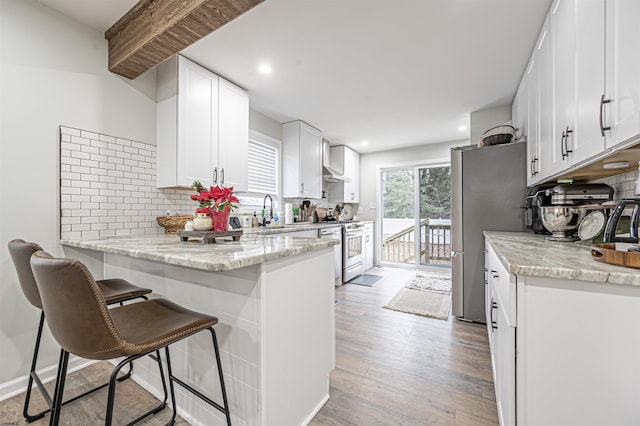 kitchen with a breakfast bar area, white cabinetry, light stone counters, light wood-type flooring, and appliances with stainless steel finishes