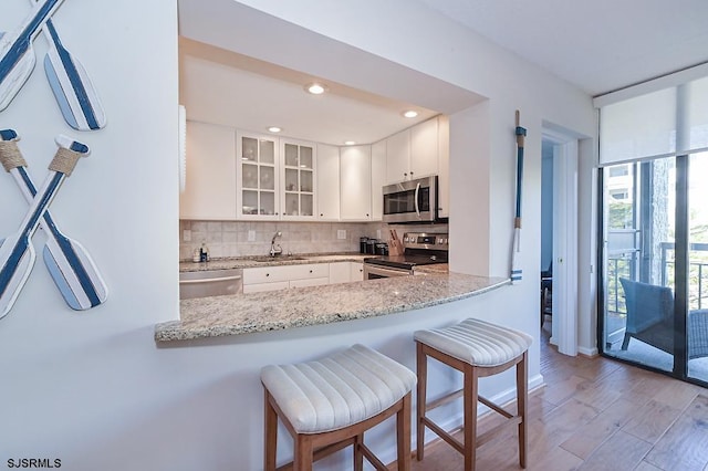 kitchen with backsplash, appliances with stainless steel finishes, kitchen peninsula, and white cabinets