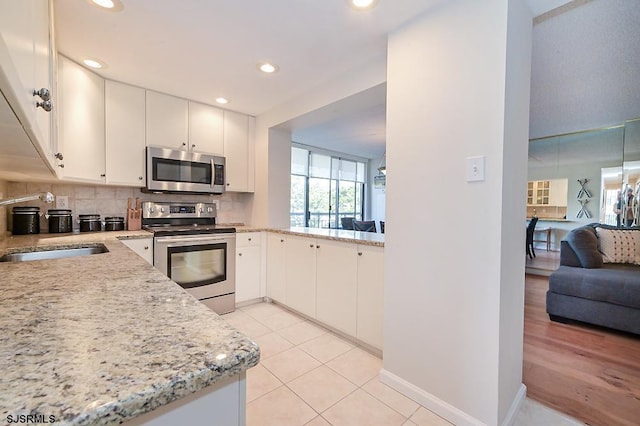 kitchen featuring sink, appliances with stainless steel finishes, white cabinetry, light stone countertops, and decorative backsplash