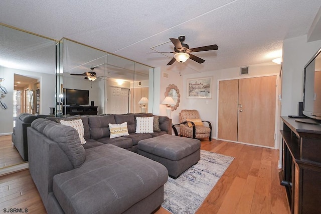 living room featuring ceiling fan, light hardwood / wood-style flooring, and a textured ceiling