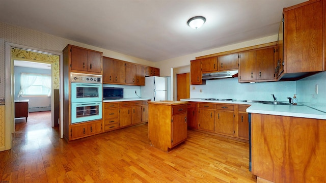 kitchen with sink, white appliances, baseboard heating, a center island, and light wood-type flooring