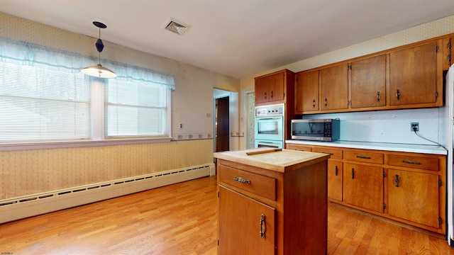 kitchen with a kitchen island, multiple ovens, a baseboard radiator, hanging light fixtures, and light wood-type flooring