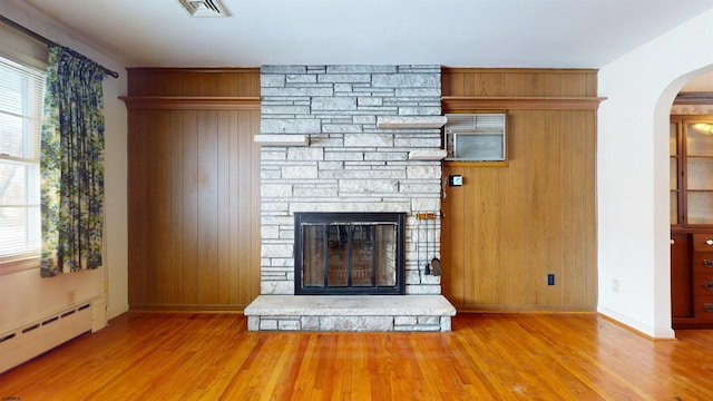 unfurnished living room featuring a baseboard heating unit, hardwood / wood-style flooring, a fireplace, and wooden walls