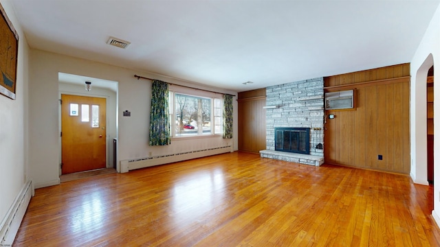 unfurnished living room with baseboard heating, a healthy amount of sunlight, a stone fireplace, and light wood-type flooring