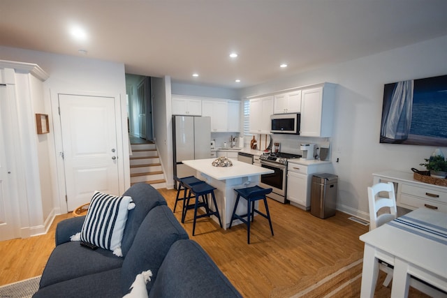 kitchen with appliances with stainless steel finishes, a breakfast bar, white cabinetry, a center island, and light hardwood / wood-style flooring