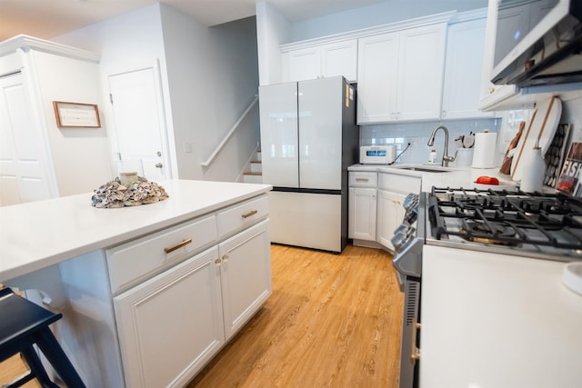 kitchen featuring sink, white cabinetry, light hardwood / wood-style flooring, stainless steel appliances, and backsplash