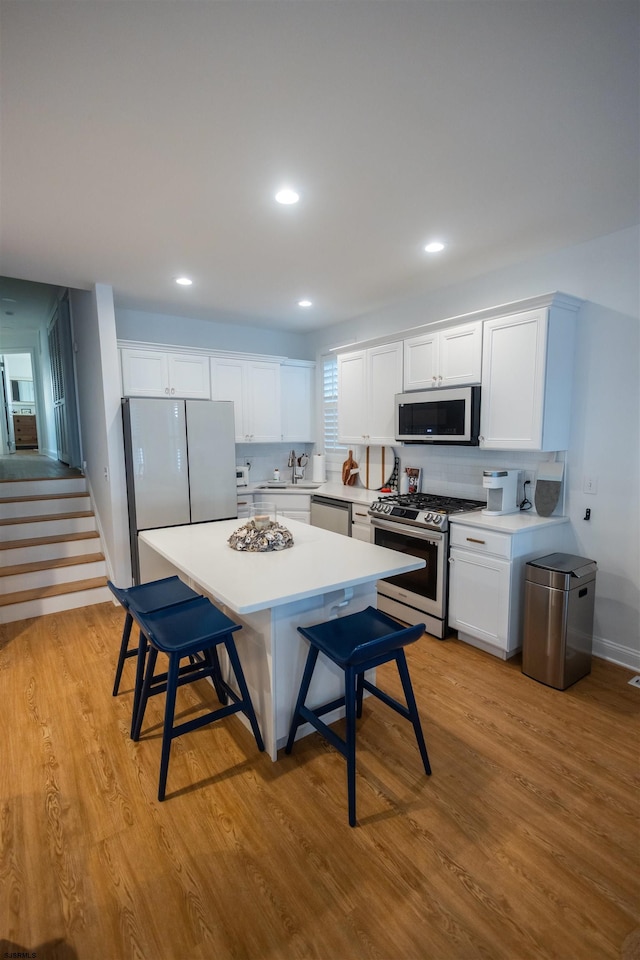 kitchen with sink, light hardwood / wood-style flooring, stainless steel appliances, white cabinets, and a kitchen bar