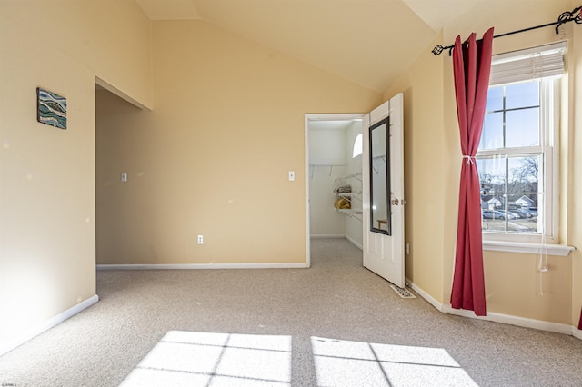 empty room featuring a wealth of natural light, vaulted ceiling, and carpet flooring