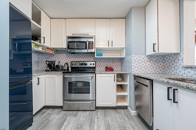 kitchen with white cabinetry, light hardwood / wood-style flooring, appliances with stainless steel finishes, light stone countertops, and backsplash