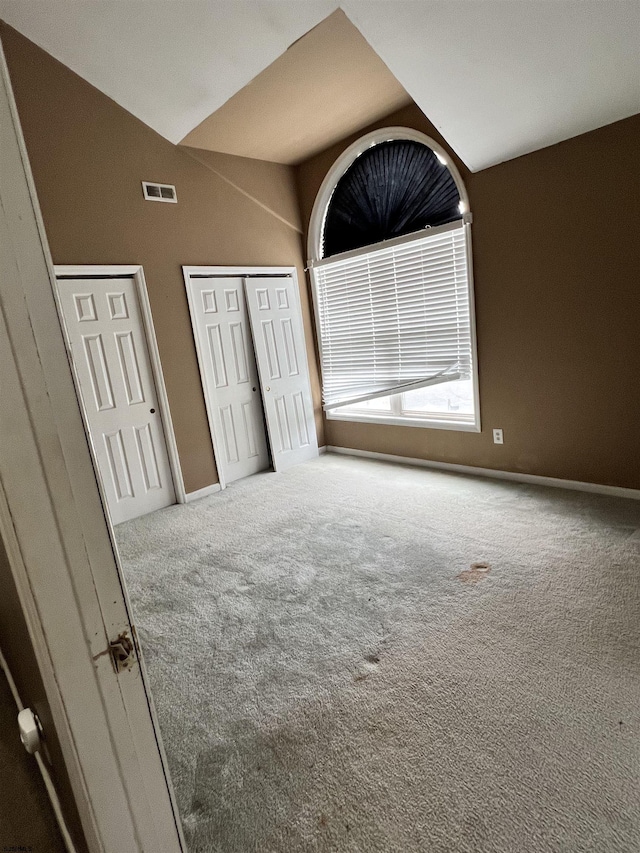 unfurnished bedroom with multiple closets, lofted ceiling, and carpet