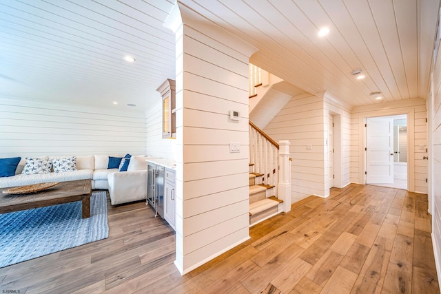 hall with wood ceiling, beverage cooler, wooden walls, and light wood-type flooring