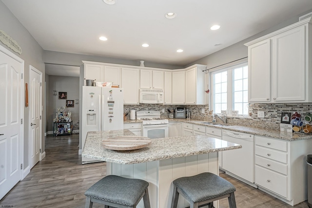 kitchen with sink, a breakfast bar area, a center island, white appliances, and white cabinets