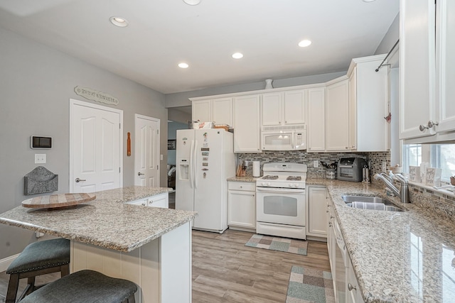 kitchen with sink, white appliances, white cabinetry, light stone countertops, and a kitchen bar