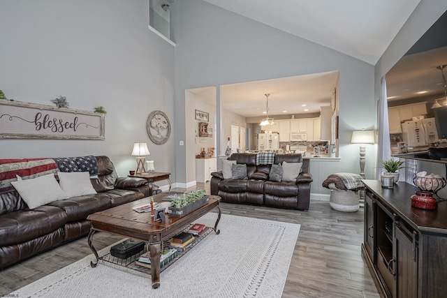 living room featuring high vaulted ceiling, a chandelier, and light wood-type flooring