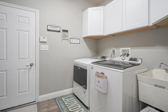 clothes washing area with sink, washer and clothes dryer, hardwood / wood-style floors, and cabinets